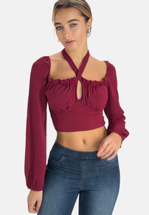Burgunderfarbener Crop-Top mit puffärmel, gerafftem Ausschnitt und einem Schlüssellochdetail in der Mitte. Kombiniert mit blauen High-Waist-Jeans.