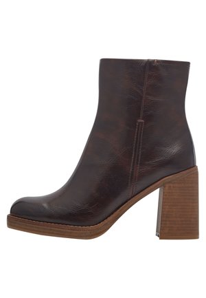 Bottine en cuir synthétique marron avec un bout arrondi et une finition texturée, présentant un talon en bois et un détail de couture le long de la semelle.