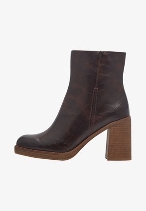 Bottine en cuir synthétique marron avec un bout arrondi et une finition texturée, présentant un talon en bois et un détail de couture le long de la semelle.
