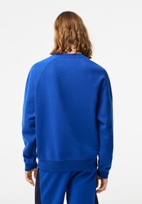 Niebieska bluza wykonana z miękkiego materiału, z okrągłym dekoltem, ściągaczami na mankietach oraz luźnym krojem. Gładka faktura, bez widocznych wzorów.