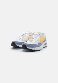 Nike-sneakers i vitt, grått och orange. Har mesh- och syntetiska material, rundad tå, vadderad krage och synlig Air-dämpning.