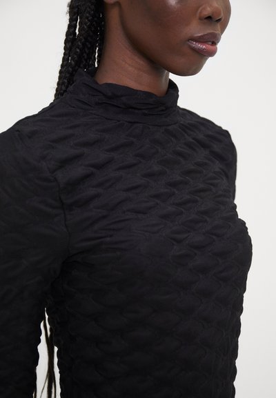 Black long-sleeve top with a high collar, featuring a textured, wave-like pattern throughout the fabric. Smooth finish and fitted silhouette.