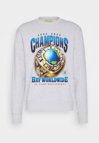 Felpa grigia con una grande grafica di un anello di campionato con un globo blu. Il testo include "CAMPIONI" e "HUF WORLDWIDE 20 ANNI DI ANNIVERSARIO."