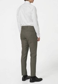 Pantalons à carreaux gris avec une coupe ajustée, portés avec une chemise blanche et des chaussures de ville noires, vus de dos.