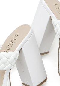 Witte hoge hak sandalen met een chunky blokhak, geweven bandontwerp, een gladde textuur en een beige binnenzool met metallic letters.
