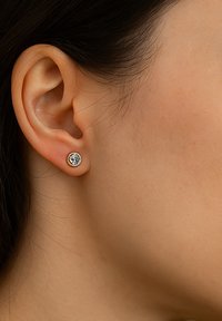 Goldene Steckerohrringe besitzen ein klares Schmuckstück in der Mitte, das in einer runden Fassung eingesetzt ist. Die glatte Metalloberfläche ergänzt den brillant geschliffenen Edelstein.