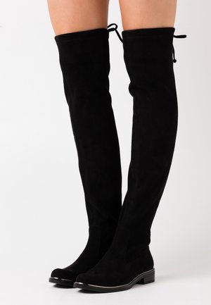 Bottes noires montantes au-dessus du genou en daim, présentant une texture lisse, un bout arrondi et une semelle plate avec un subtil accent métallique le long du bord.