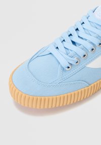 Light blue canvas sneaker with textured upper and a contrasting rubber sole. Features flat laces and metal eyelets.