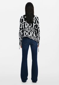 Top bianco e nero con grandi motivi di testo, abbinato a jeans svasati blu scuro. Il top presenta dei cordini sulle maniche.