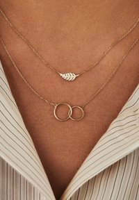 Colliers en or plaqué avec un pendentif en forme de feuille et un design de cercles entrelacés. Chaîne fine au toucher lisse, portée contre la peau.