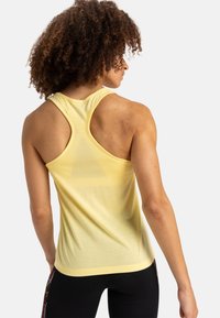 Gelbes ärmelloses Sportoberteil mit Racerback-Design. Hergestellt aus glattem Stoff mit leichtem Glanz und lockerer Passform, die eine schlichte Ästhetik präsentiert.