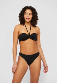 Svart bikini-sett med et strapless, vridd bandeau-top med tynne nakkebånd og lavt skjørt. Glatt stoff med minimalistisk design.