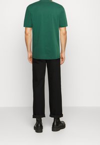 Grön bomulls T-shirt med rund halsringning, tillsammans med svarta vida byxor med uppvikta ärmar och kraftiga svarta ankelstövlar.