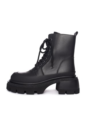 Botte de combat en cuir noir avec semelle épaisse à crampons, lacets sur le devant, haut de la cheville et poignet à l'arrière sur fond blanc.
