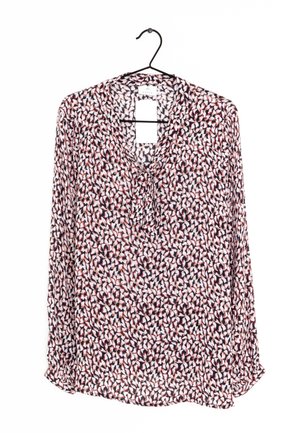 Blusa a manica lunga con motivo astratto di petali neri, bianchi e rossi appesa a una gruccia nera su sfondo bianco.