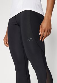 Sorte athletic leggings med en tettsittende design, med mesh-paneler og en liten logo. Jevn tekstur med kontrastfargede sømdetaljer.