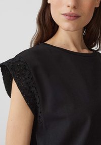 Zwarte katoenen top met geborduurde korte mouwen met uitsnijdingen. Ronde halslijn, zachte textuur en relaxte pasvorm.