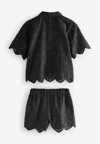 Completo in cotone nero composto da top e pantaloni corti con bordi scallop, modelli ad occhio di pernice e disegni floreali testurizzati. Maniche corte e vita elastica.