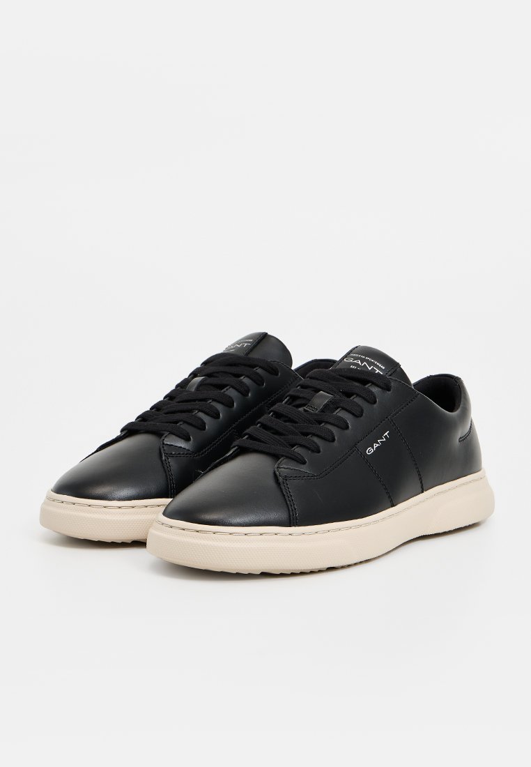 Sneakers in pelle nera con finitura liscia, punta tonda e suola in gomma beige a contrasto. Presentano lacci neri e un logo di lato.