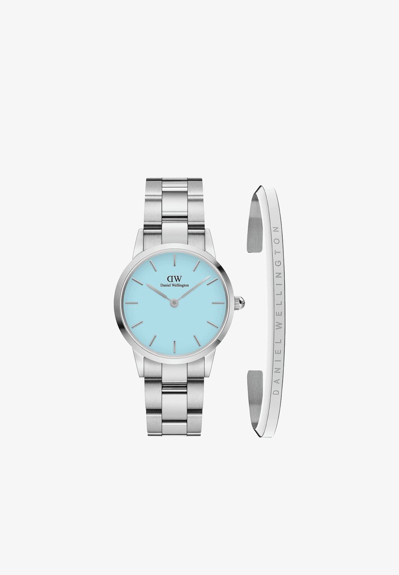 Reloj de acero inoxidable plateado con una esfera redonda de un azul claro. Presenta marcadores de hora delgados y una pulsera elegante y pulida. Incluye un puño plateado.