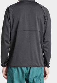 Långärmad, mörkgrå tröja med textilstruktur och hög krage. Har raglanärmar och rak fåll, tillsammans med teal cargobyxor.