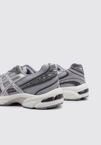 Baskets de sport grises avec une tige en mesh, des accents en daim superposés, une semelle intermédiaire blanche rembourrée et une semelle extérieure en caoutchouc noir.