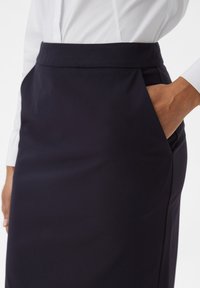 Marineblauwe pencil skirt met een gladde textuur en een zijzak. Gecombineerd met een wit shirt, is de tailleband gestructureerd en op maat gemaakt.