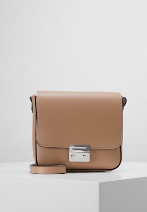 Pequeño bolso bandolera de cuero beige con cierre de metal plateado y correa ajustable, colocado sobre un pedestal blanco contra un fondo gris.
