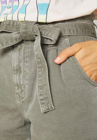 Pantalones cortos de color gris claro, de cintura alta, con un cinturón de tela atado, que cuentan con bolsillos laterales y un acabado texturizado sutil.