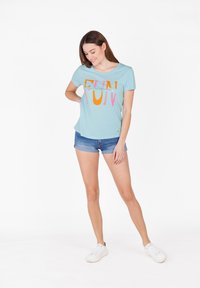 Camiseta de mangas cortas de color azul claro con un vibrante gráfico de "FUN" en naranja y rosa; combinada con pantalones cortos de mezclilla y zapatillas blancas.