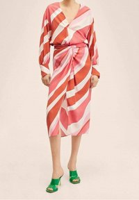 Abito avvolgente a maniche lunghe con strisce diagonali rosa, rosse e bianche, annodato in vita. Abbinato a tacchi aperti verdi.