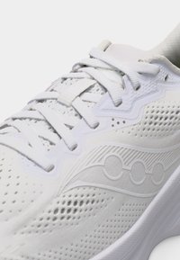 Λευκό αθλητικό παπούτσι με υφασμάτινο πλέγμα υφής στην επάνω πλευρά, λευκά κορδόνια δεμένα σε φιόγκο και διακριτικό ανάγλυφο λογότυπο στο πλάι.