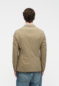 Ανοιχτό καφέ κομμένο σακάκι με δομημένο σχέδιο, διάτρητους γιακάδες και μανίκια με τρία κουμπιά, σε συνδυασμό με φθαρμένο μπλε τζιν.