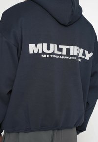 Felpa con cappuccio blu navy con grande logo bianco "MULTIPLY" sul retro, maniche lunghe e orlo a coste. Tessuto morbido e strutturato con vestibilità rilassata.