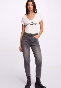 Maglietta bianca a collo a V con la scritta "In Love" in paillettes nere, abbinata a jeans grigi a vita alta e stivaletti neri. Design casual e aderente.