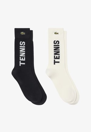Coppia di calzini crew bianco e nero con la parola "TENNIS" stampata verticalmente e un piccolo logo coccodrillo vicino al bordo.
