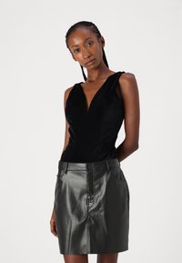 Schwarzer ärmelloser Bodysuit mit tiefem V-Ausschnitt und glatter Textur, kombiniert mit einem enganliegenden schwarzen Leder-Minirock mit Fronttaschen.