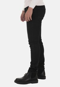 Black skinny jeans with a smooth texture, a mid-rise fit, and five pockets. Paired with black leather ankle boots featuring a cleated sole.
