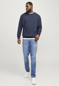 Marine crewneck sweatshirt met ribbelmanchetten, gecombineerd met lichtblauwe jeans en witte sneakers. Glad stofstructuur; ontspannen pasvorm.