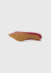 Scarpa con tacco alto a punta in vernice fucsia lucida, caratterizzata da un dettaglio a strappo sulla parte anteriore e una suola in gomma beige testurizzata.