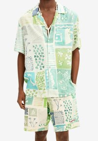 Set van kortærmelig overhemd en korte broek in licht linnen, met groene en blauwe patronen, geometrische vormen en grafische bloemmotieven.