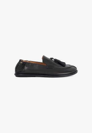 Mocassin à enfiler en cuir noir avec des pompons sur le dessus, bout arrondi, petit talon et doublure intérieure beige, présenté de profil sur un fond blanc.
