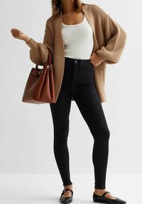 Beige stickad cardigan, vit linne, svarta högmidjade jeans, brun handväska och svarta platåskor. Cardigan har en lös passform och ett strukturerat mönster.