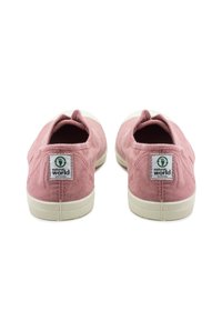 Zapatillas de lona rosas sin cordones con una textura suave, que presentan una suela de goma blanca y una etiqueta con el logo en el talón. Diseño minimalista.