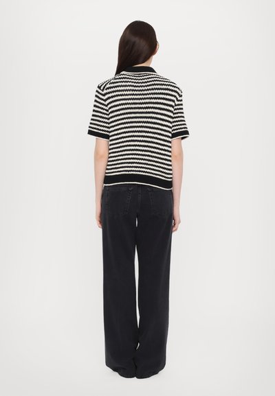 Randig stickad tröja i svart och vitt med korta ärmar och krage, i kombination med vida svarta jeans. Fokusera på de texturerade tygmönstren.