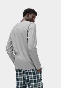 Gray long-sleeve top with a crew neckline and ribbed texture, paired with plaid pajama bottoms featuring green, navy, and white colors.