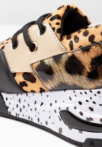 Baskets chunky avec fourrure imprimée léopard, œillets en cuir beige, lacets noirs et semelle blanche avec motif tacheté noir.