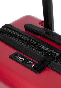 Valigia rigida rossa con zip nera, lucchetto a combinazione e manico estensibile. Texture liscia e design elegante con dettagli robusti.