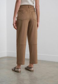 Pantalons en coton marron avec un design à jambes droites, dotés de poches arrière, de détails de couture et associés à des ballerines à motifs.