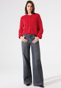 Rote, flauschige Strickjacke mit Rundhalsausschnitt und vorderen Knöpfen, kombiniert mit hoch-taillierten, weit geschnittenen, dunkelgrauen Jeans. Minimalistisches Design.